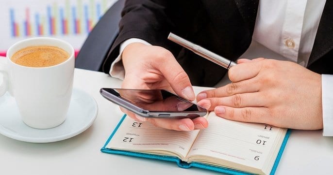 hands holding pen and phone at desk with datebook