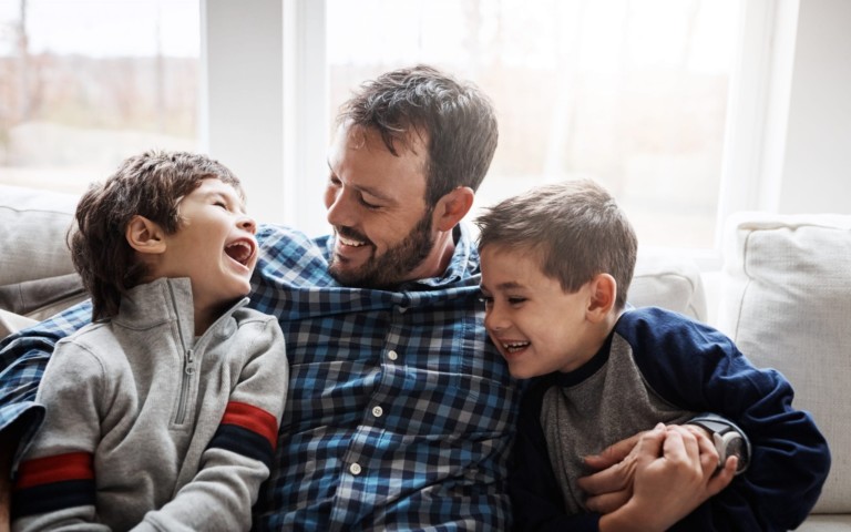 father holding two laughing sons on couch
