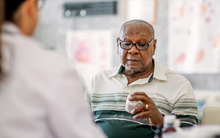 older man looking at medicine bottle with pharmacist