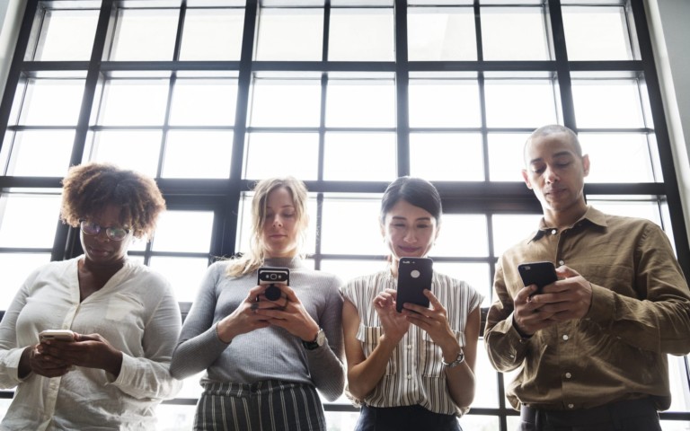 four people in business dress looking at phones in front of window