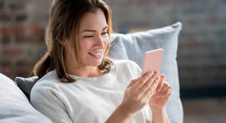 smiling woman sitting on couch holding phone