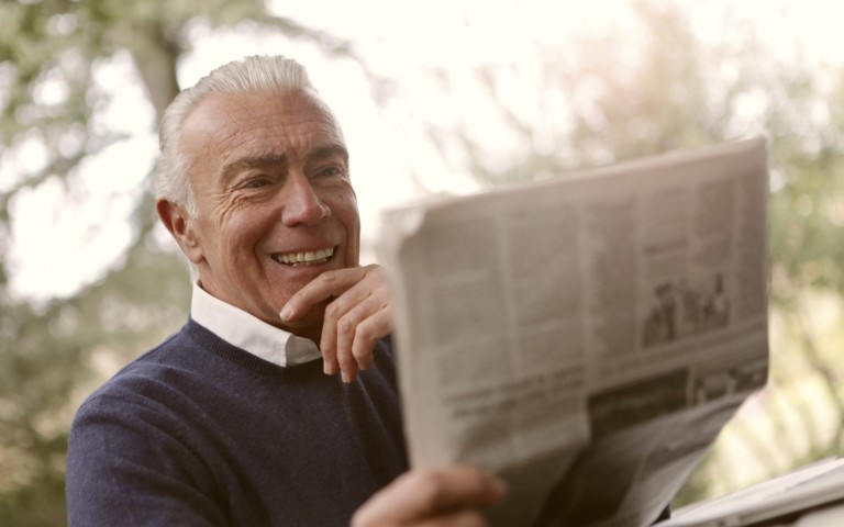 smiling older man reading newspaper