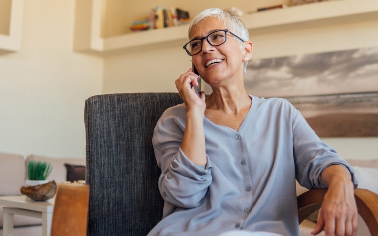smiling older woman sitting in desk chair talking on phone