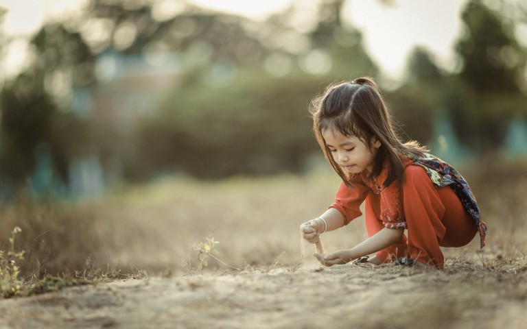 little girl outside letting sand fall through hand