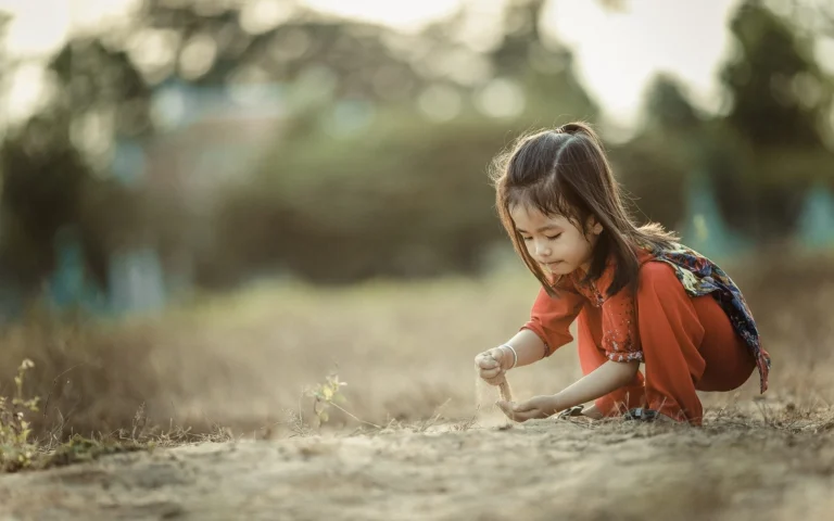 little girl outside letting sand fall through hand
