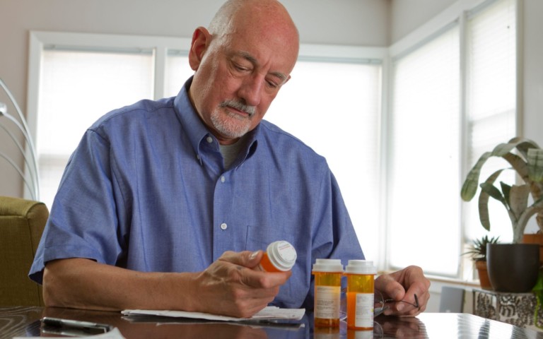 older man reading prescription bottles