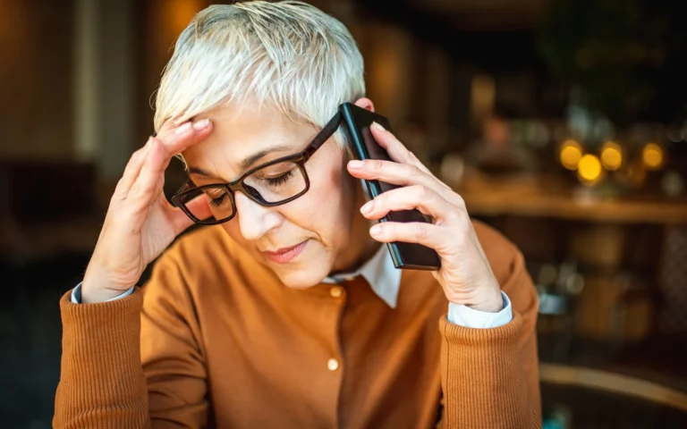 older woman with phone to her ear holding head in hand