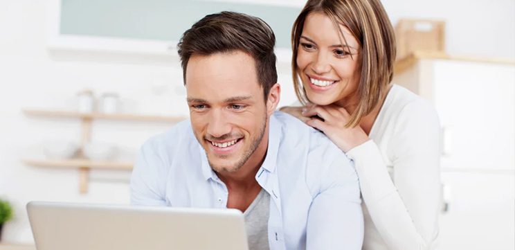 smiling young couple using laptop to schedule online