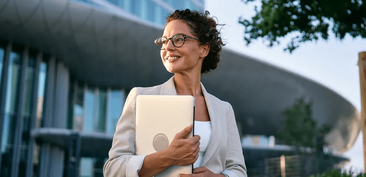Senior women healthcare executive outdoors holding laptop, representing women's leadership in healthcare