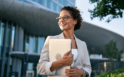 Senior women healthcare executive outdoors holding laptop, representing women's leadership in healthcare