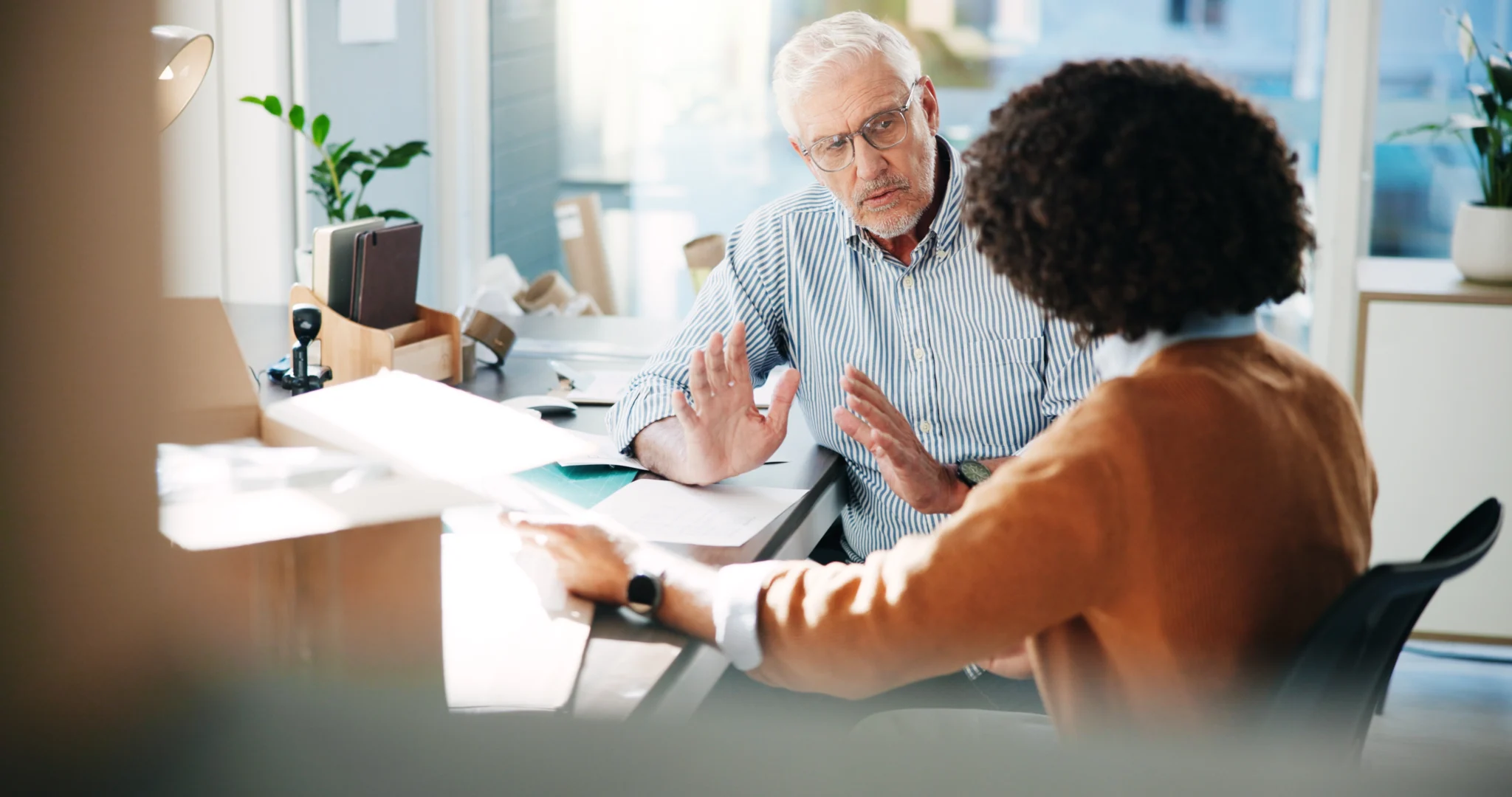 Two colleagues talking across a desk while reviewing printed documents