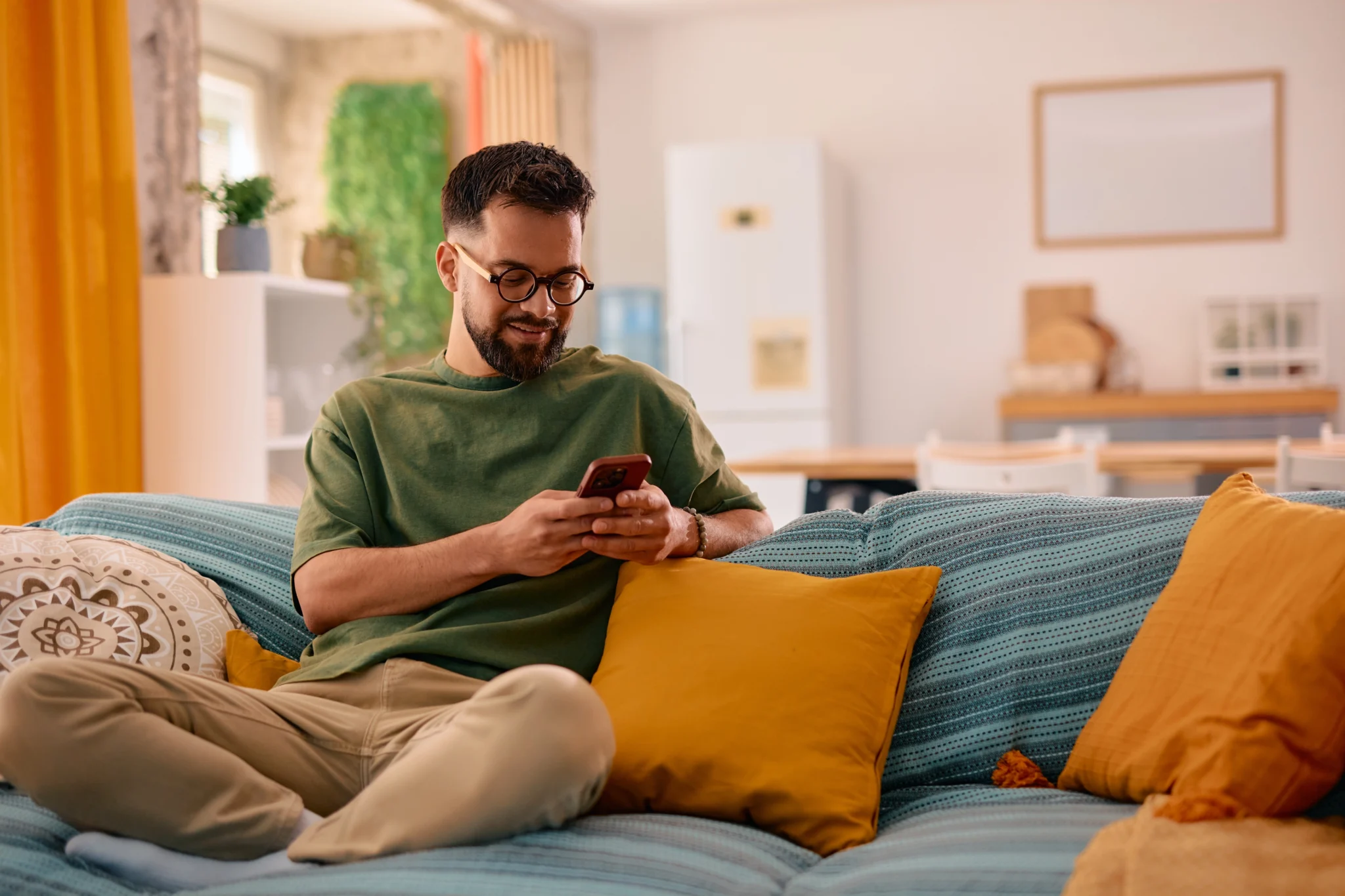 Man sitting on a couch at home smiling while using his phone