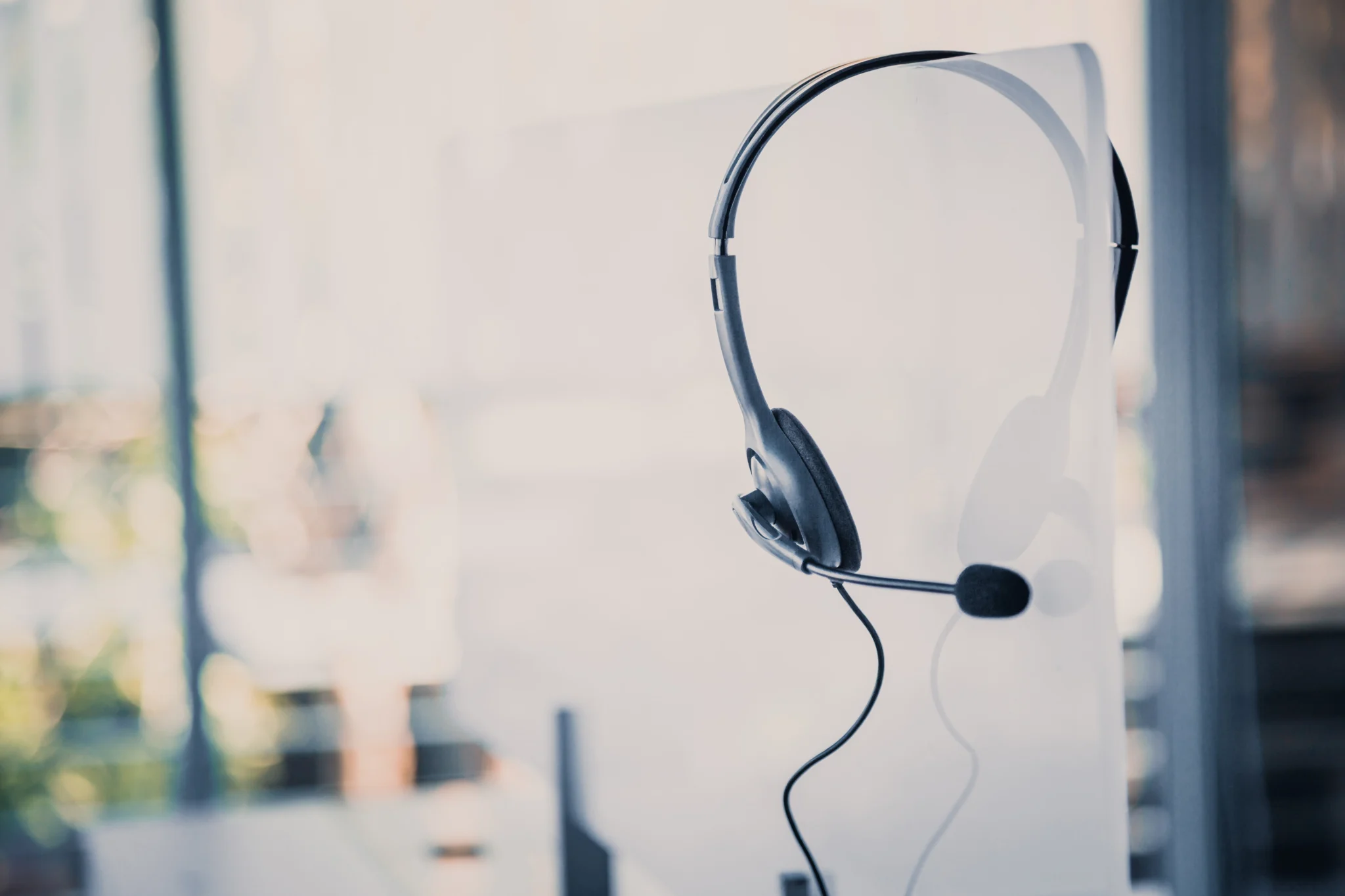 Headset with microphone hanging on the edge of a desk partition in a bright office