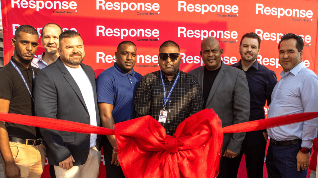 Group of seven people standing behind a large red ribbon and bow at a ribbon-cutting event, posing in front of a red “Response by Carenet Health” branded backdrop.